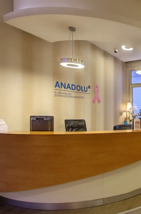 Modern hospital reception area with curved front desk, waiting chairs, and a wall-mounted TV in a softly lit lobby.